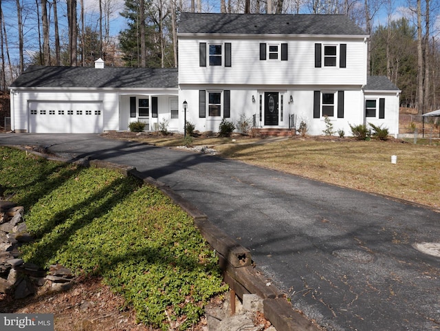 colonial home featuring driveway, an attached garage, a chimney, and a front lawn