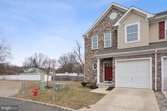 view of front of home with a shingled roof, a front lawn, fence, stone siding, and driveway