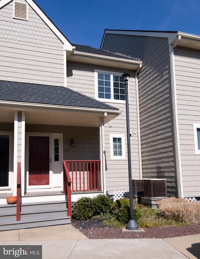 entrance to property with central AC, a porch, and roof with shingles