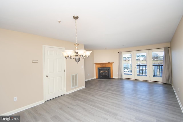 unfurnished living room featuring visible vents, a notable chandelier, baseboards, and wood finished floors