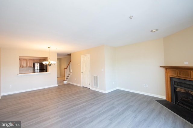 unfurnished living room featuring visible vents, a fireplace with flush hearth, wood finished floors, baseboards, and stairs