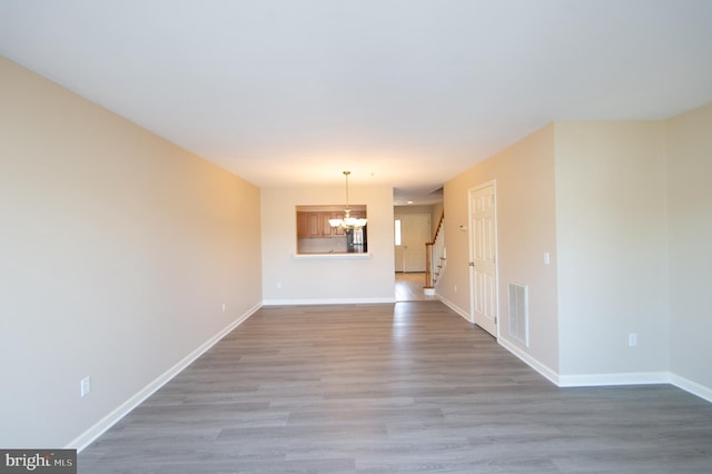 unfurnished living room with a notable chandelier, wood finished floors, visible vents, baseboards, and stairway