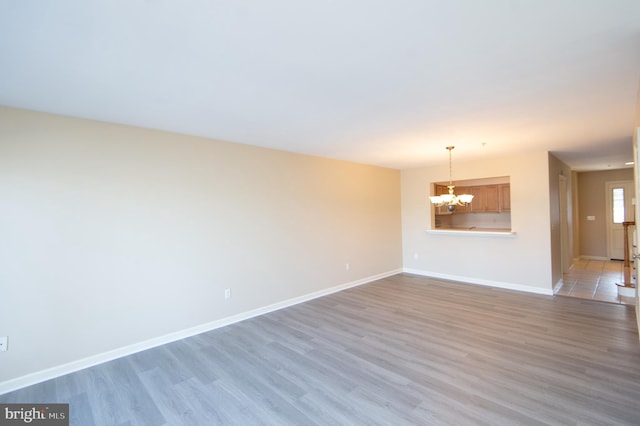 unfurnished room featuring baseboards, light wood finished floors, and an inviting chandelier