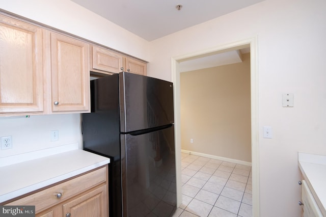 kitchen with light tile patterned floors, freestanding refrigerator, light countertops, and light brown cabinetry