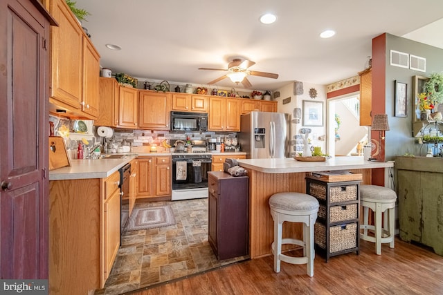 kitchen featuring a breakfast bar area, light countertops, decorative backsplash, a ceiling fan, and black appliances