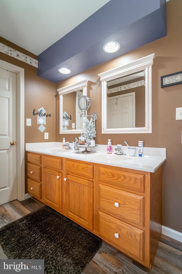 bathroom with wood finished floors, a sink, baseboards, and double vanity