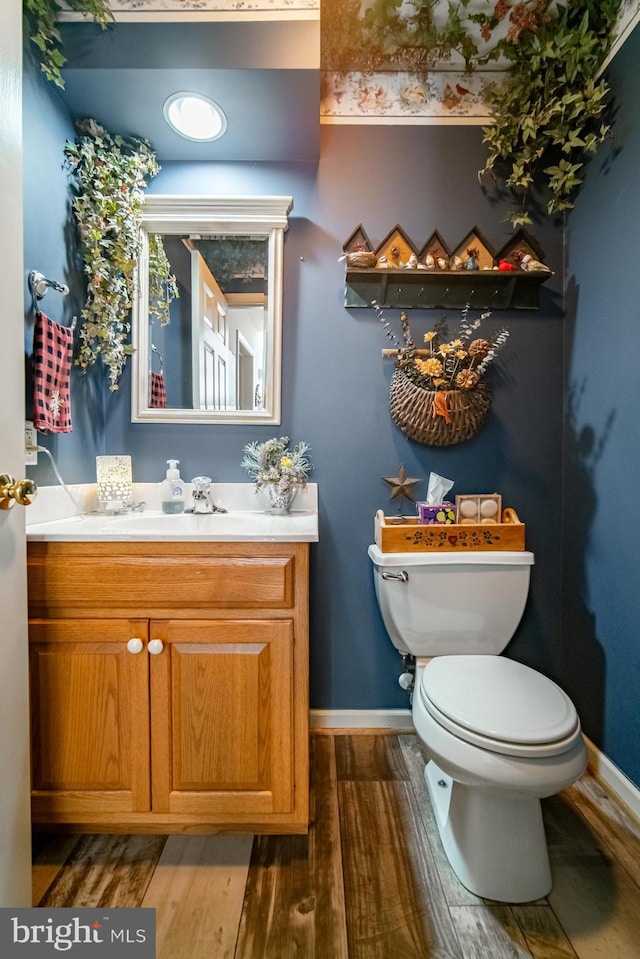 bathroom featuring toilet, baseboards, wood finished floors, and vanity