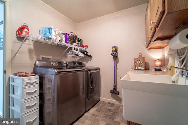 laundry area featuring cabinet space, washing machine and dryer, stone finish flooring, a sink, and baseboards