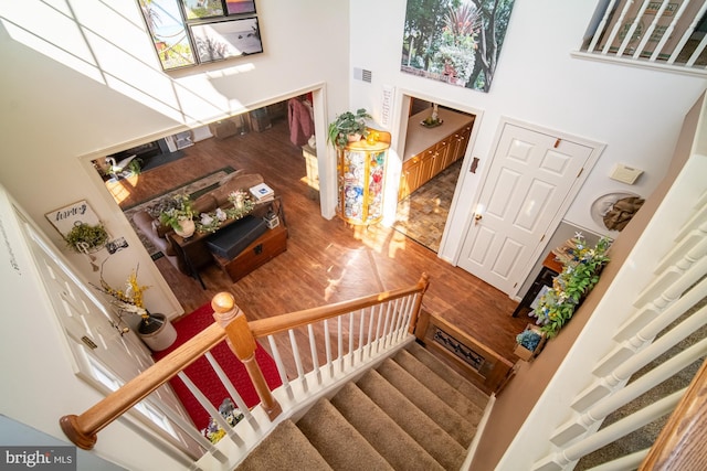 stairs with a towering ceiling, visible vents, and wood finished floors