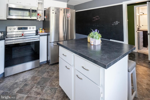 kitchen featuring appliances with stainless steel finishes, dark countertops, a center island, and white cabinets