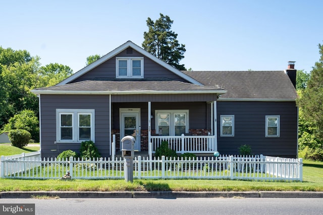 bungalow-style home with covered porch, a fenced front yard, a chimney, and roof with shingles