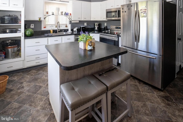 kitchen with stainless steel appliances, dark countertops, white cabinets, a sink, and a kitchen breakfast bar