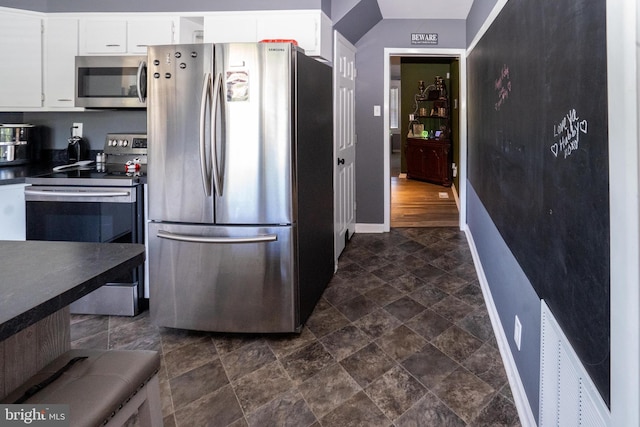 kitchen featuring baseboards, white cabinets, dark countertops, appliances with stainless steel finishes, and stone finish flooring