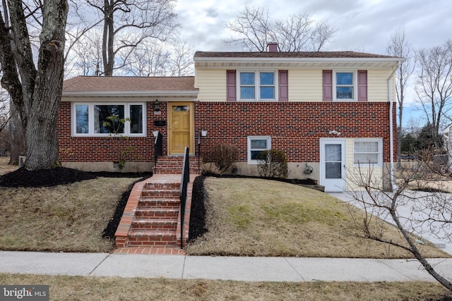 tri-level home with a chimney, a front lawn, and brick siding