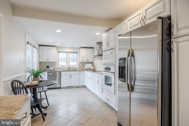 kitchen with light tile patterned floors, stainless steel appliances, white cabinets, wall chimney exhaust hood, and tasteful backsplash