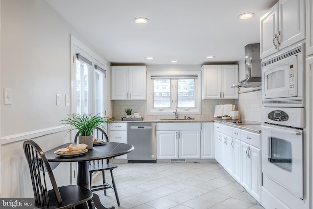 kitchen featuring decorative backsplash, white cabinets, a sink, wall chimney range hood, and white appliances