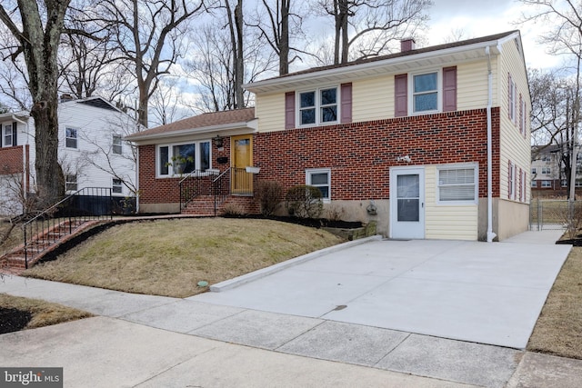 tri-level home featuring driveway, brick siding, a chimney, fence, and a front yard