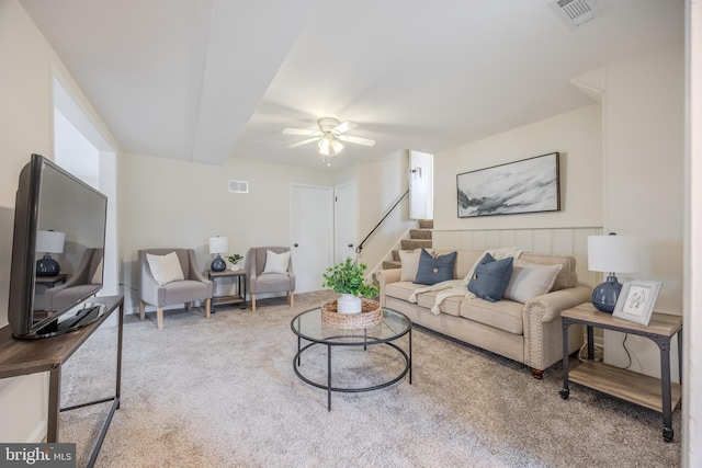 carpeted living area with stairway, visible vents, and a ceiling fan