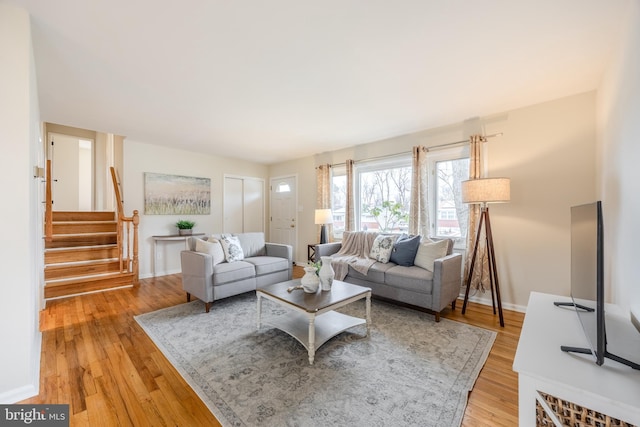 living area featuring baseboards, light wood finished floors, and stairs