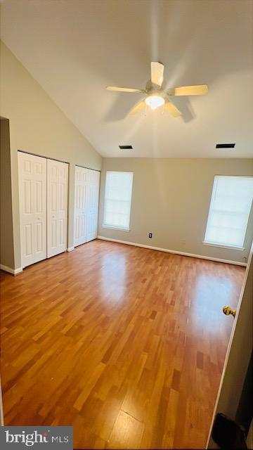 unfurnished bedroom with vaulted ceiling, wood finished floors, two closets, and visible vents