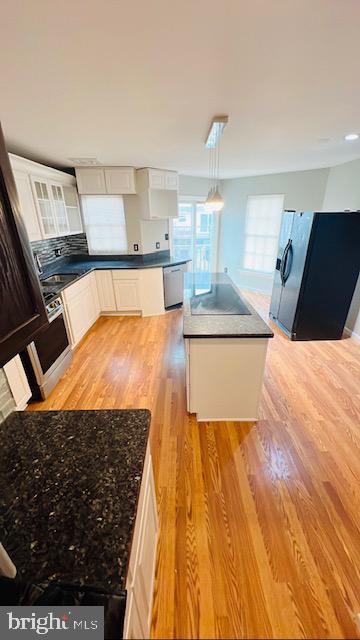 kitchen with white cabinetry, stainless steel dishwasher, light wood-type flooring, black refrigerator with ice dispenser, and dark countertops