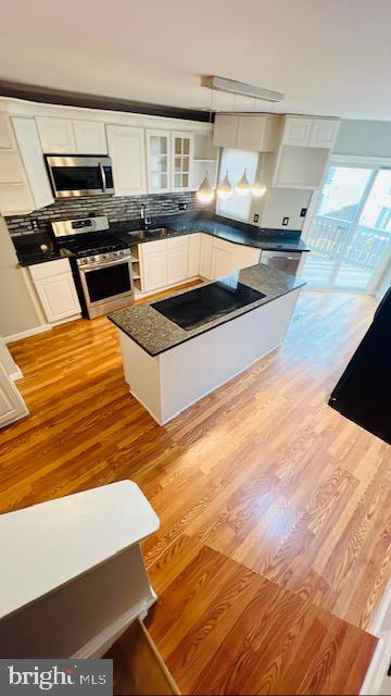 kitchen featuring light wood-style flooring, stainless steel appliances, white cabinetry, dark countertops, and glass insert cabinets