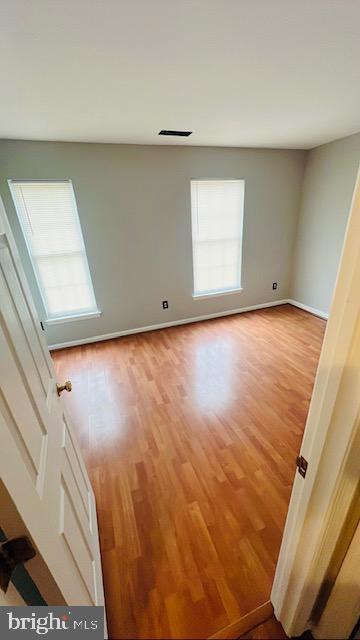 empty room with visible vents, wood finished floors, a wealth of natural light, and baseboards