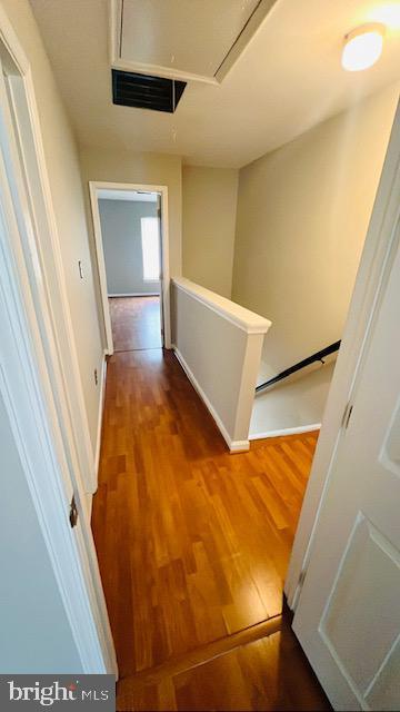 hallway featuring attic access, visible vents, an upstairs landing, and wood finished floors