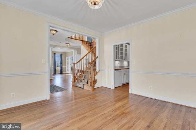 spare room featuring stairs, crown molding, light wood-style flooring, and baseboards