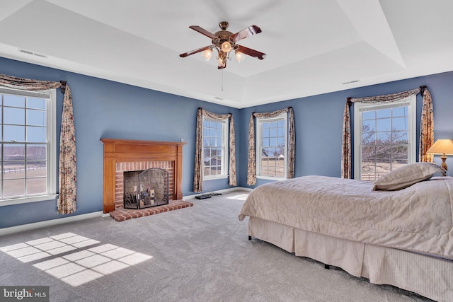 carpeted bedroom with visible vents, baseboards, a tray ceiling, a fireplace, and ceiling fan