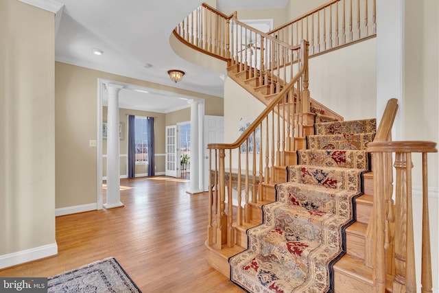 stairs with ornamental molding, wood finished floors, a high ceiling, decorative columns, and baseboards