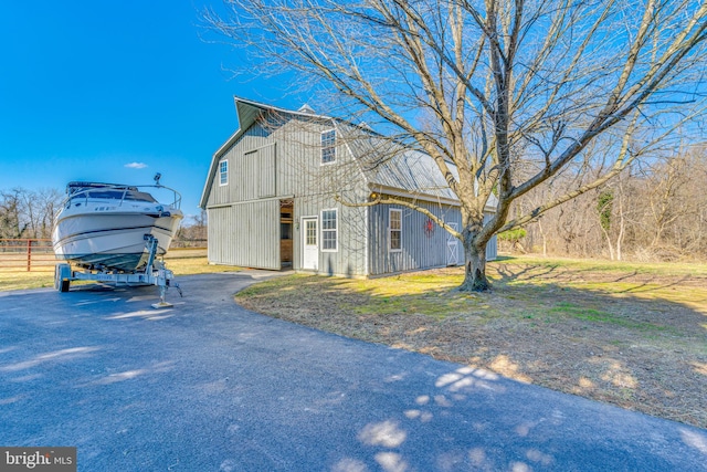 view of property exterior featuring a barn, fence, aphalt driveway, a gambrel roof, and an outbuilding