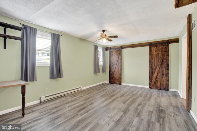 unfurnished bedroom with a textured ceiling, a barn door, a baseboard radiator, wood finished floors, and baseboards