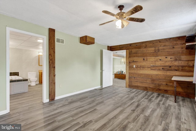 unfurnished bedroom featuring ensuite bath, wood finished floors, visible vents, and baseboards