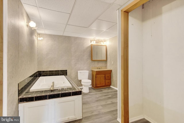 full bathroom with a tub to relax in, baseboards, toilet, wood finished floors, and a paneled ceiling