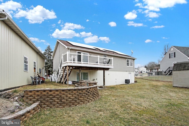 rear view of property with a lawn, stairway, roof mounted solar panels, cooling unit, and a wooden deck