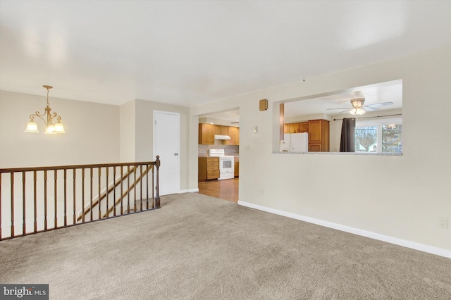 empty room with carpet, baseboards, and ceiling fan with notable chandelier