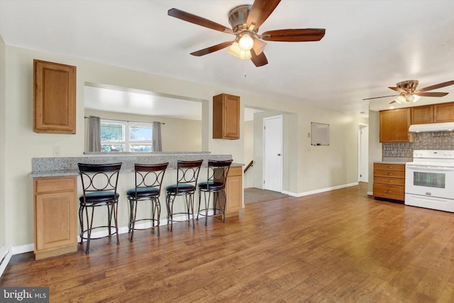 kitchen with a breakfast bar area, under cabinet range hood, wood finished floors, backsplash, and white range with electric stovetop