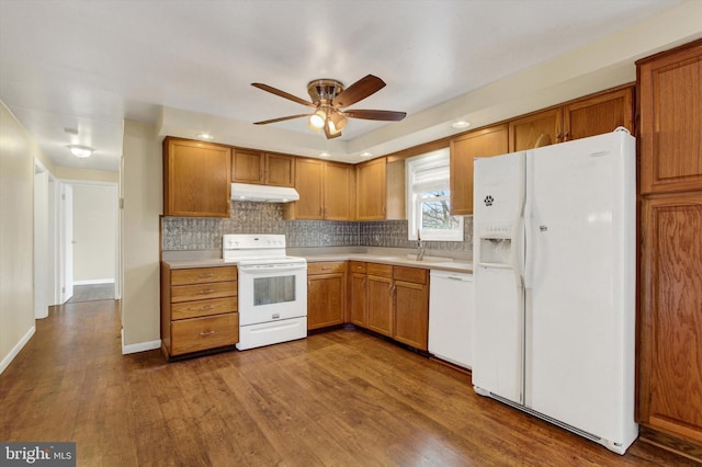 kitchen with white appliances, dark wood finished floors, light countertops, under cabinet range hood, and a sink