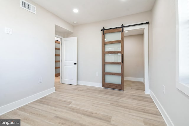 unfurnished bedroom with light wood-type flooring, visible vents, baseboards, and a barn door