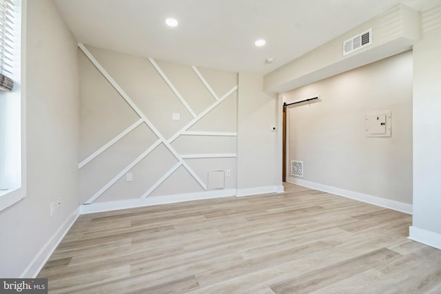 spare room with recessed lighting, visible vents, a barn door, wood finished floors, and baseboards