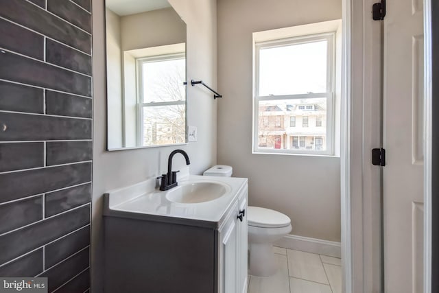 half bath featuring toilet, a healthy amount of sunlight, baseboards, and vanity