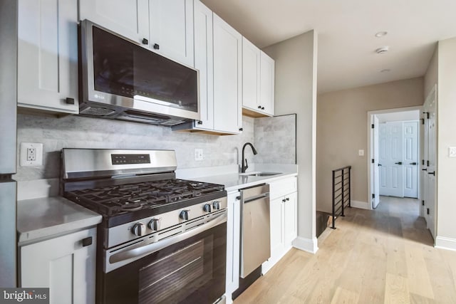 kitchen featuring decorative backsplash, appliances with stainless steel finishes, light wood-style floors, white cabinetry, and a sink