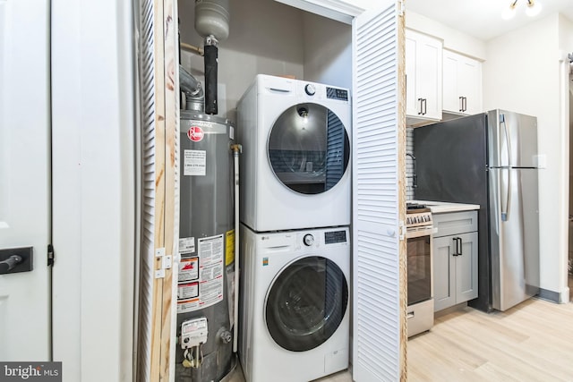 laundry room featuring water heater, laundry area, light wood finished floors, and stacked washer and clothes dryer