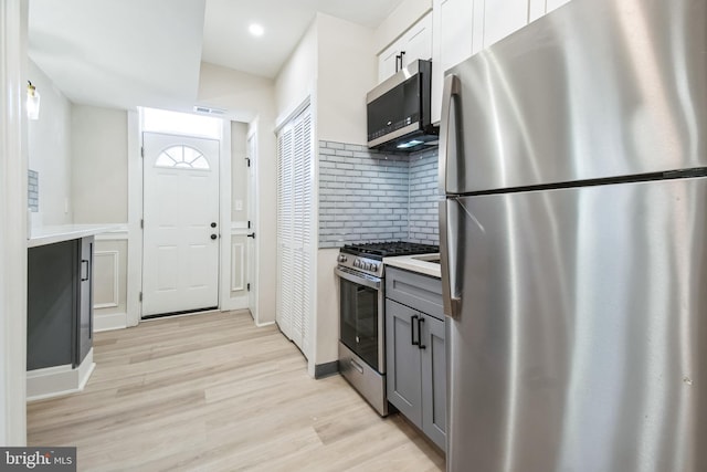 kitchen featuring light wood-style flooring, gray cabinetry, stainless steel appliances, visible vents, and decorative backsplash