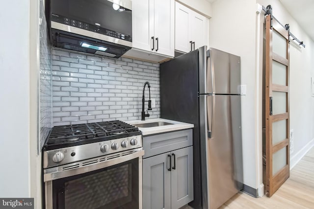 kitchen featuring a barn door, stainless steel appliances, a sink, light wood-type flooring, and decorative backsplash