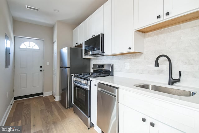 kitchen with visible vents, white cabinets, decorative backsplash, stainless steel appliances, and a sink