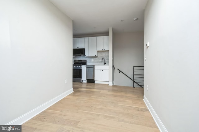 kitchen with stainless steel appliances, light countertops, backsplash, light wood-style flooring, and a sink