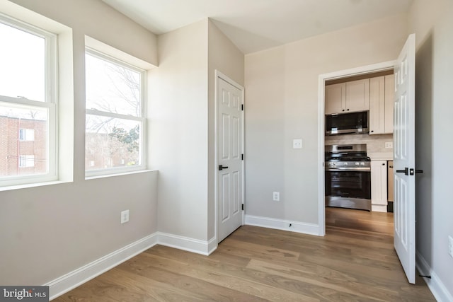 interior space with stainless steel appliances, backsplash, light wood-style flooring, and baseboards