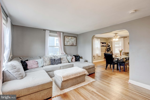 living area with light wood-type flooring, arched walkways, baseboards, and a ceiling fan